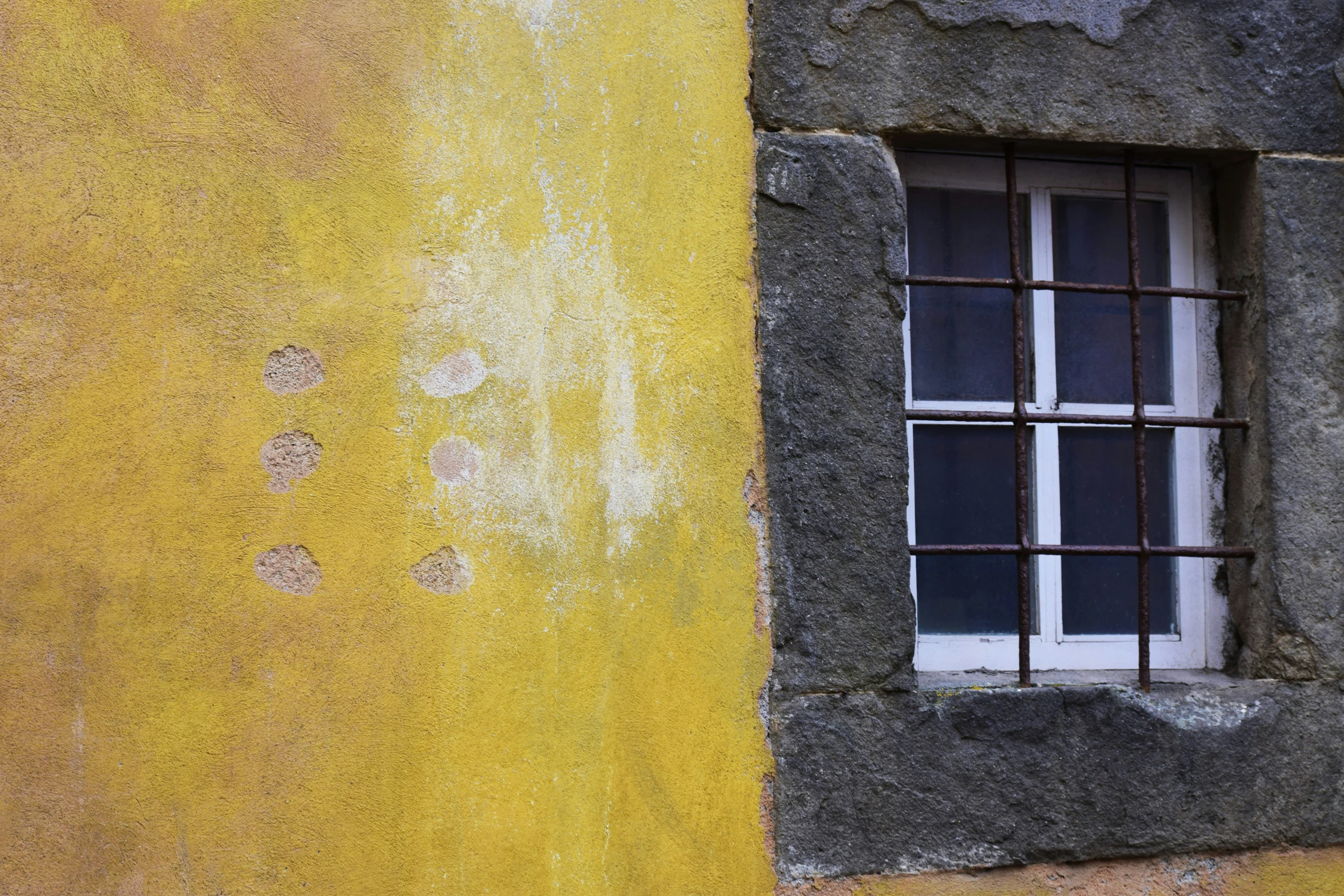 a window sits against an old yellow wall