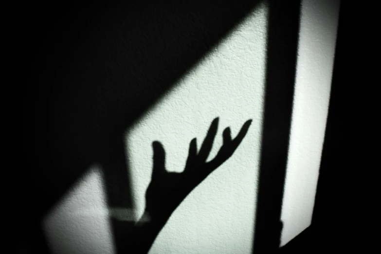 shadow of hand with arm reaching towards window on wall