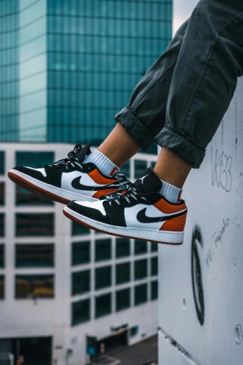person with black and orange nike shoes on the top of a white building