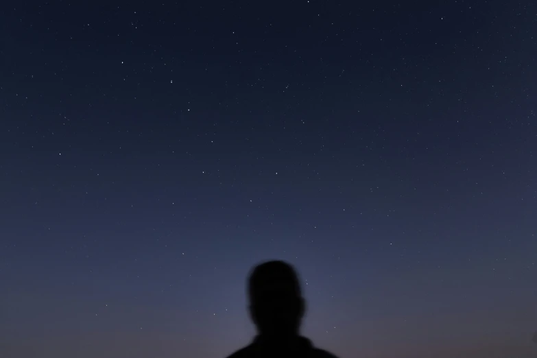 a man who is standing up with his back to the camera and arms extended in front of him are some stars in the night sky