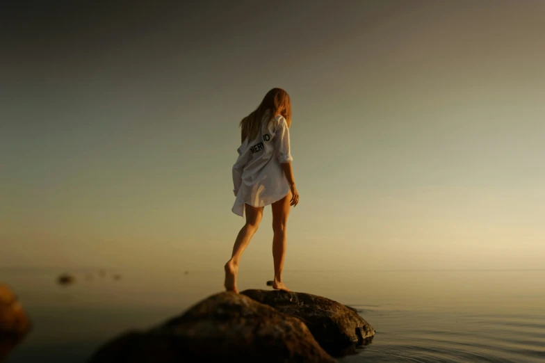 a girl on the rocks and water looks up at the sky