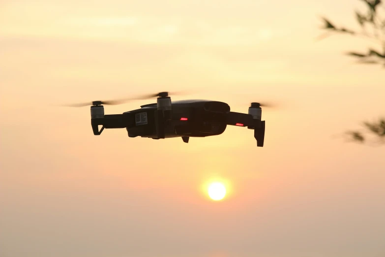 an aerial view of a black helicopter flying towards the sun