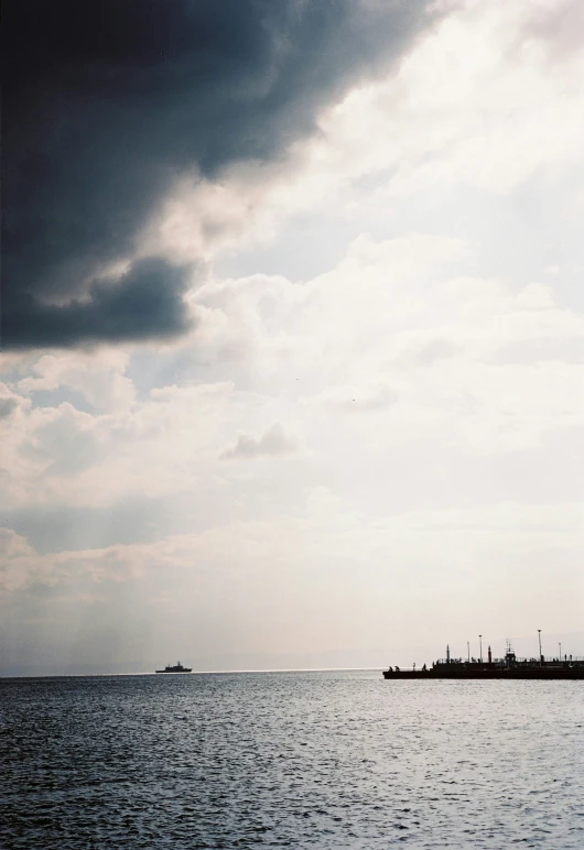 the silhouette of a ship on the ocean under dark clouds