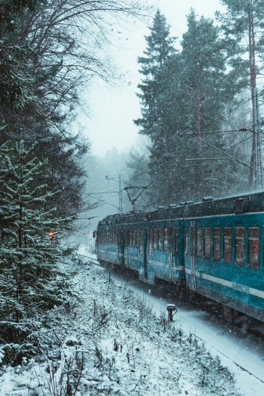 a blue train moving down the tracks in the snow