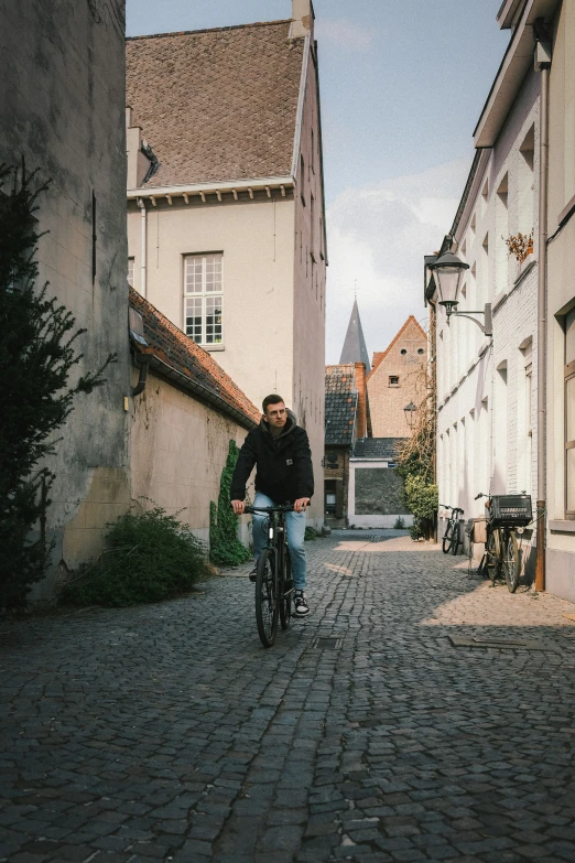 man on bicycle on cobblestone road between buildings