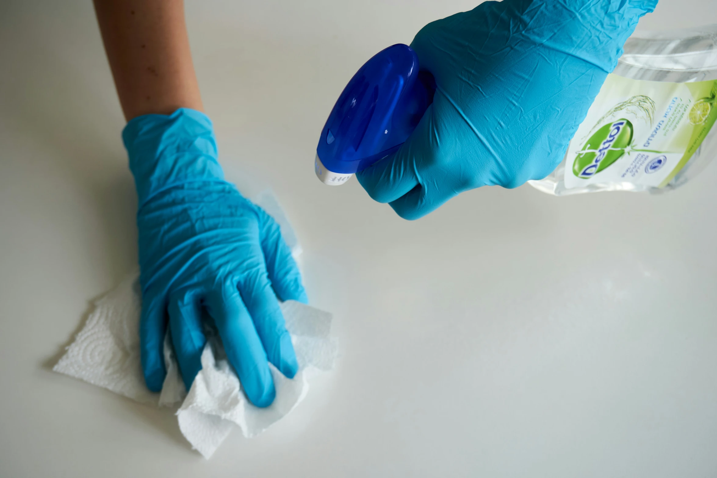 a hand wearing blue latex gloves is cleaning a table with a micro wave sponge and cloth