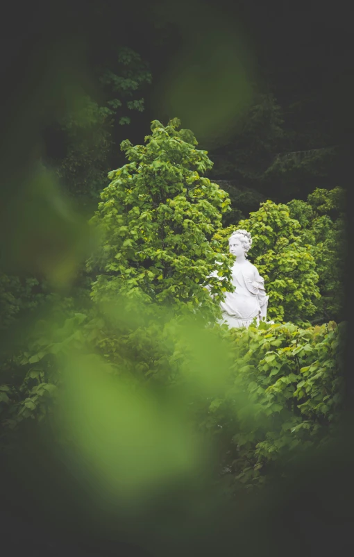 a white statue surrounded by trees with a bush nearby