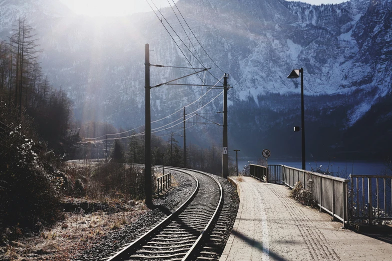 an empty train track in a mountain area with trees and a body of water