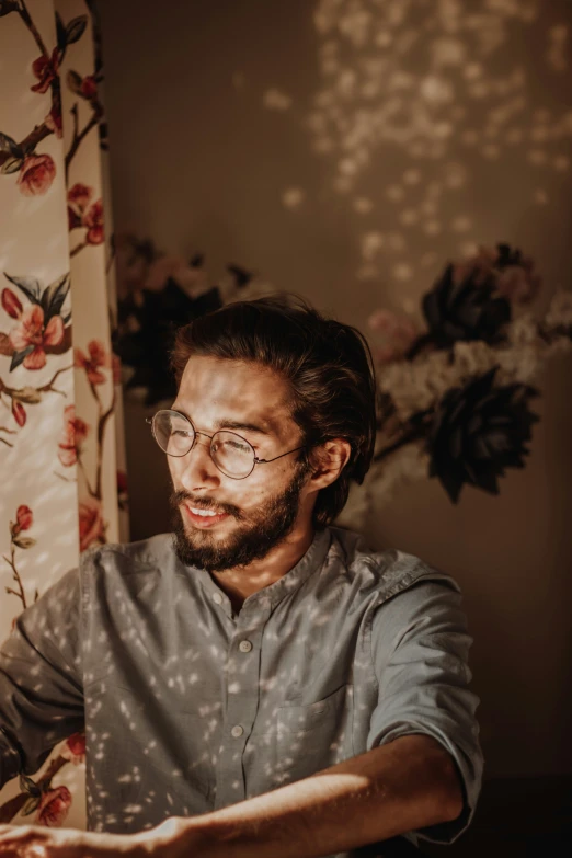 a man wearing glasses and laughing in front of floral curtains