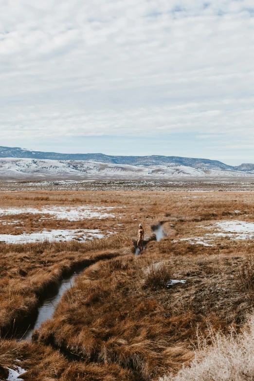 two people stand on an empty grassy plain in the background