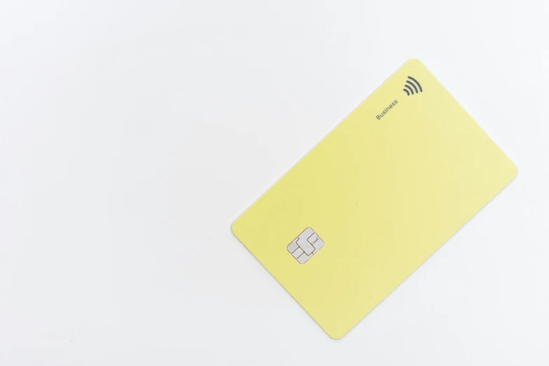 a yellow plastic credit card laying flat on top of white surface