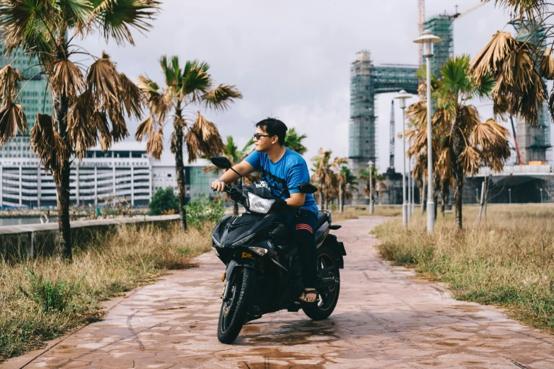 man riding a motorcycle on a pathway near palm trees