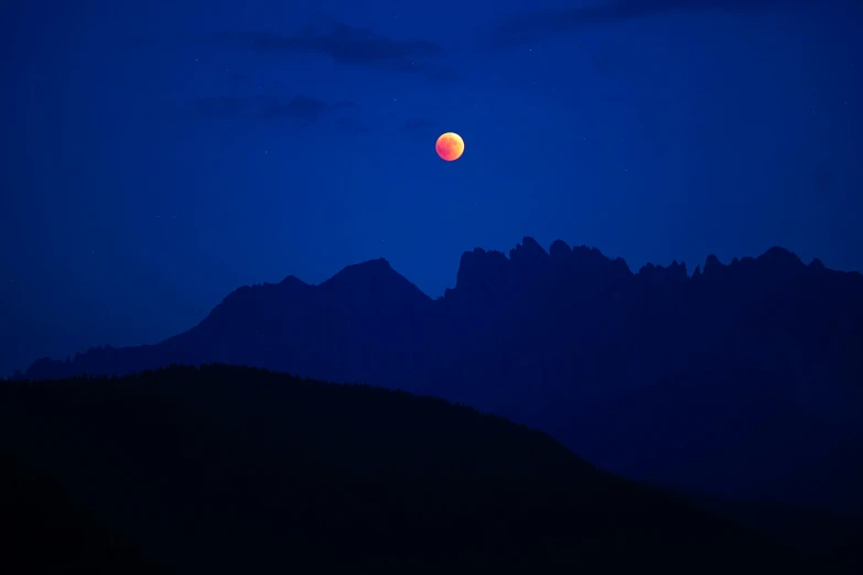 the moon is setting over the mountain tops