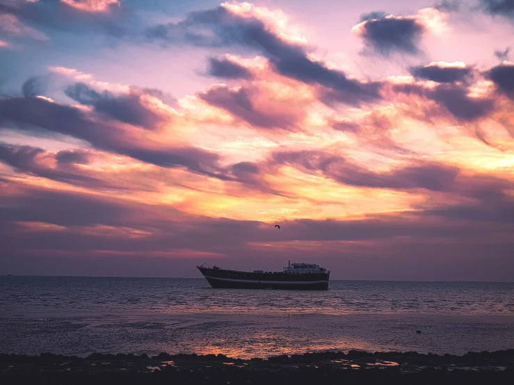 a boat sits on the ocean as the sun sets