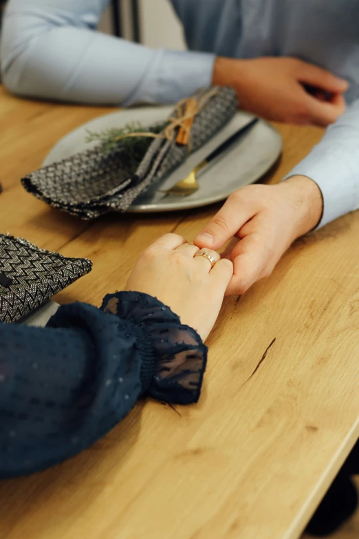 two people hold hands over a wooden table