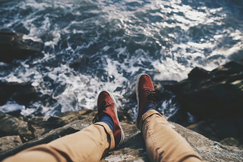 a person with red sneakers sitting near some water