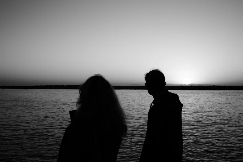 the couple is staring at the horizon as the sun sets