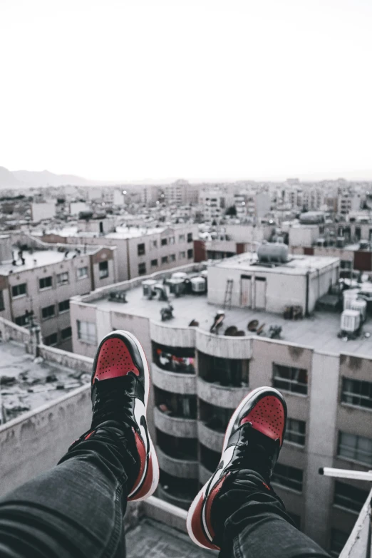 a person wearing black jeans and red shoes is looking over a cityscape