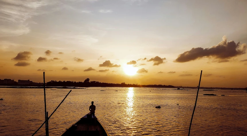 a boat sits on a calm river with the sun setting in the distance