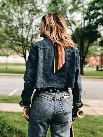 the back of a person with long hair wearing denim jacket and tie