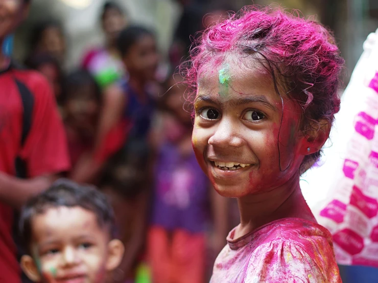 two small children smile while standing with their faces painted in red and green