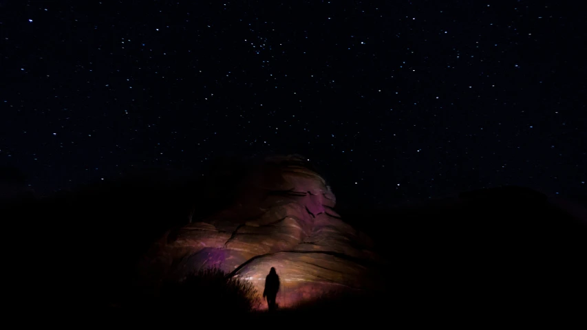 a person that is standing under a big rock