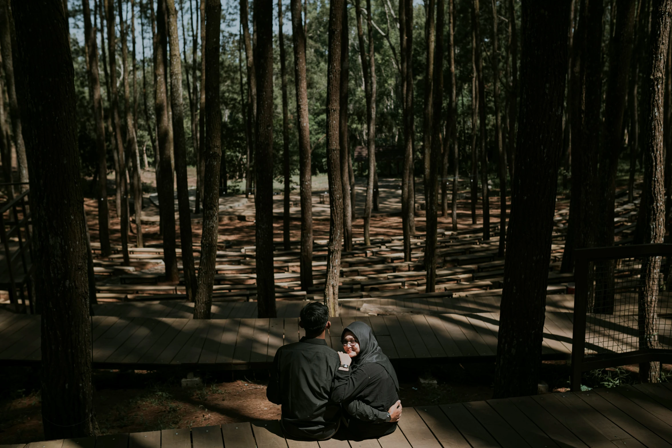 there is a man sitting on a bench in the forest talking on a phone