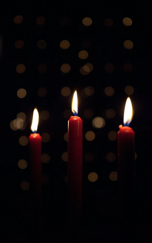 three lit candles sit in the dark with their lights turned on