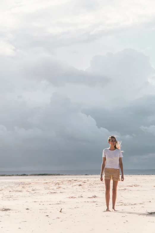 a woman with her head lowered, stands on the beach