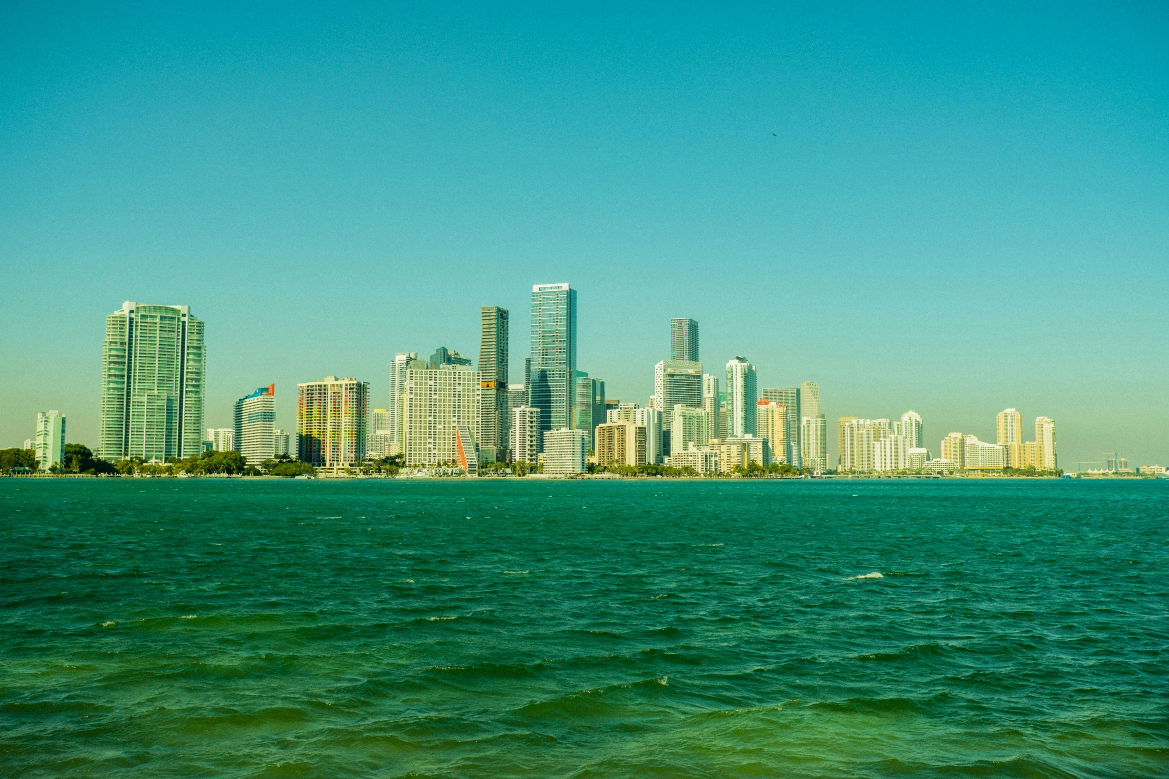 an empty boat floating on the blue water of a bay with a city in the background