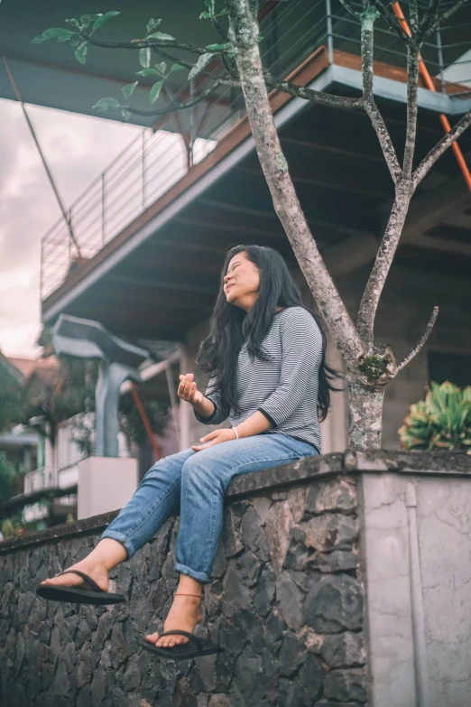 a woman sitting in front of a tree on a stone wall