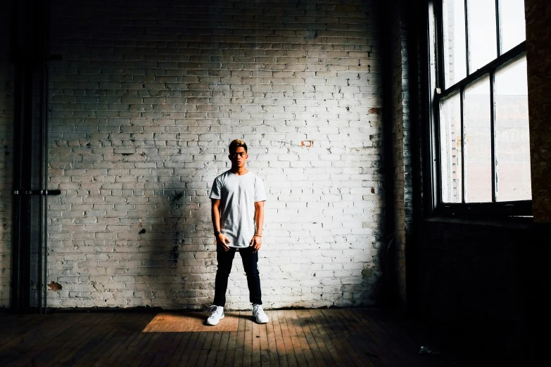 a young man standing against a white brick wall