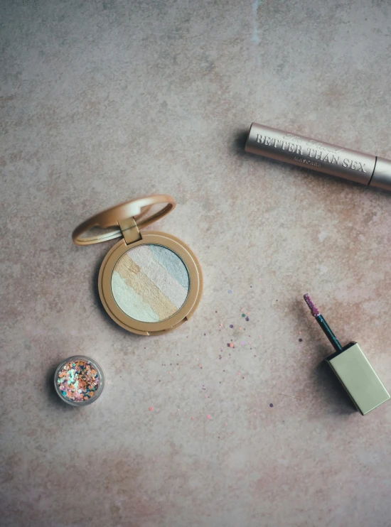 makeup is laying on the floor next to a pen, pencils and a compact