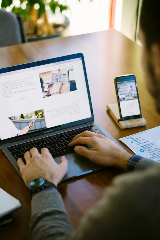 man sitting at wooden table using his laptop with other devices