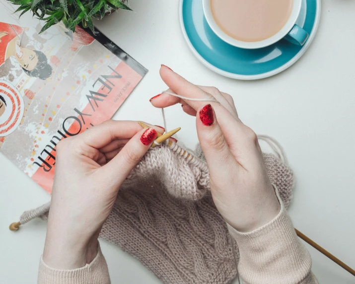 a person knitting yarn in front of a cup of coffee