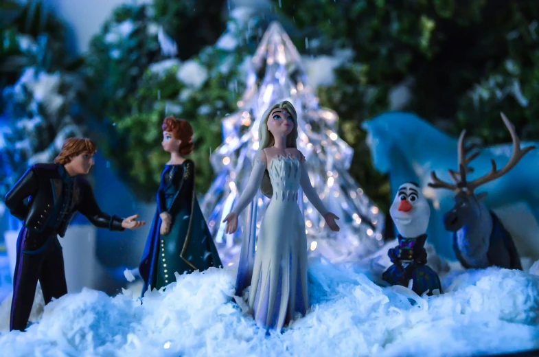 several figurines from the frozen princess, one in front of a decorated christmas tree