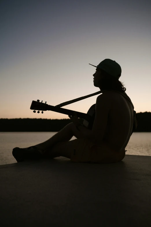 silhouetted man playing guitar on a calm lake