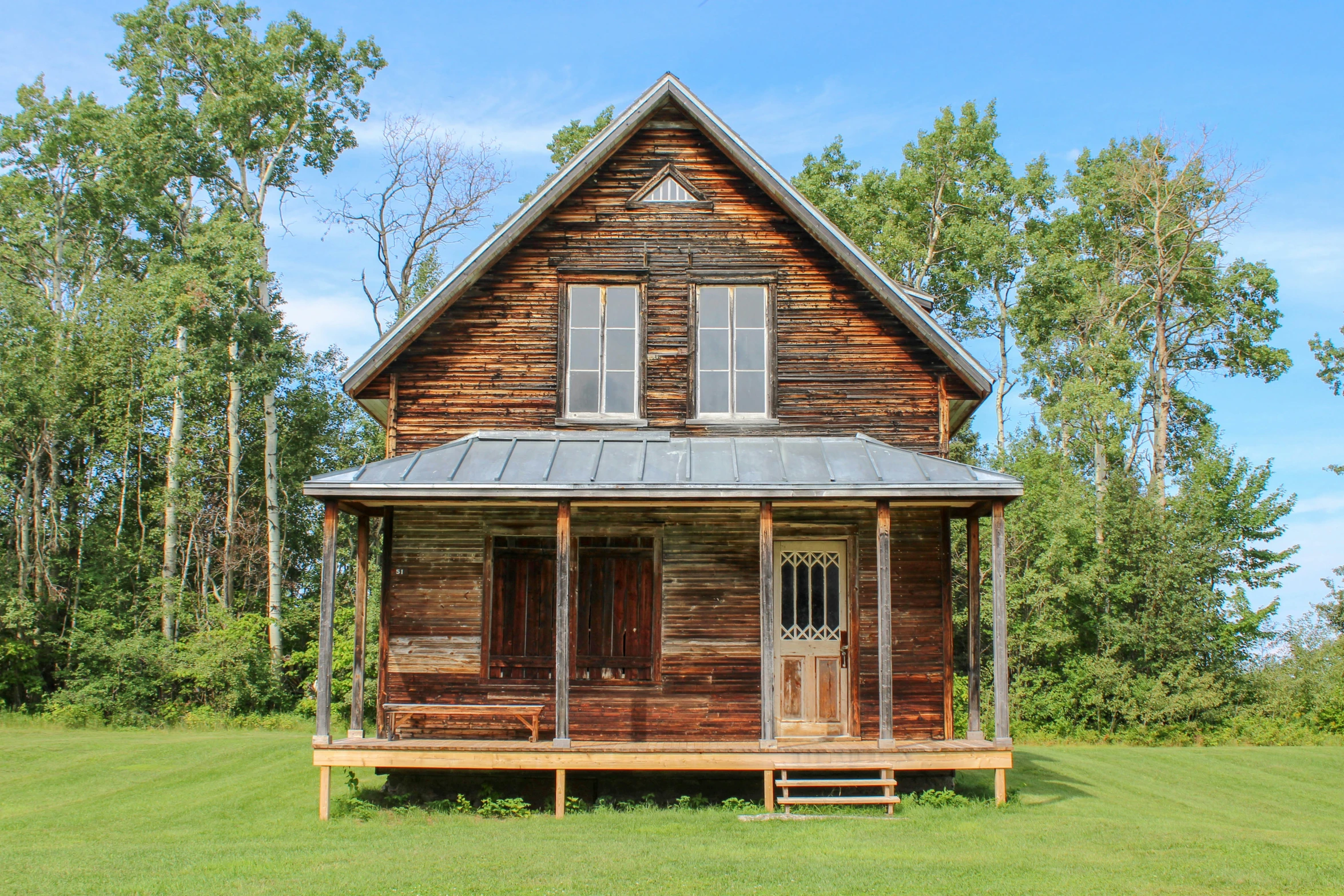 a log cabin sits in a green pasture surrounded by woods