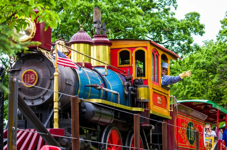the man is waving to the small colorful train