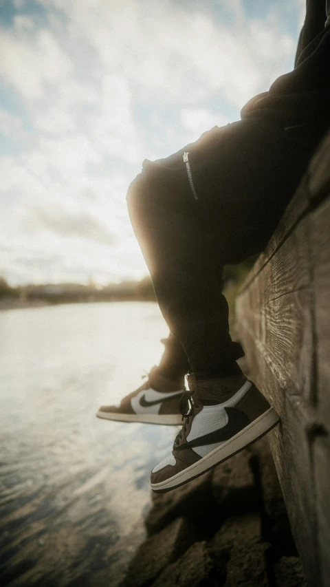 a person's legs and feet, as he sits on the wall over the water