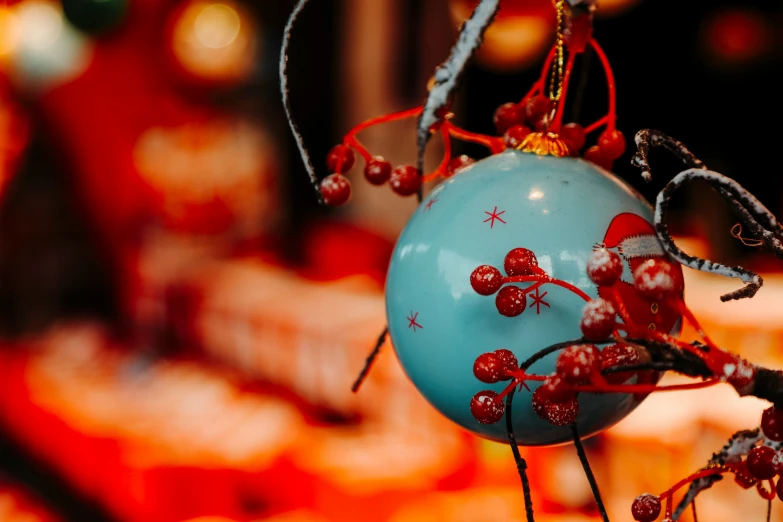 a blue ball hanging from a tree with red berries on it