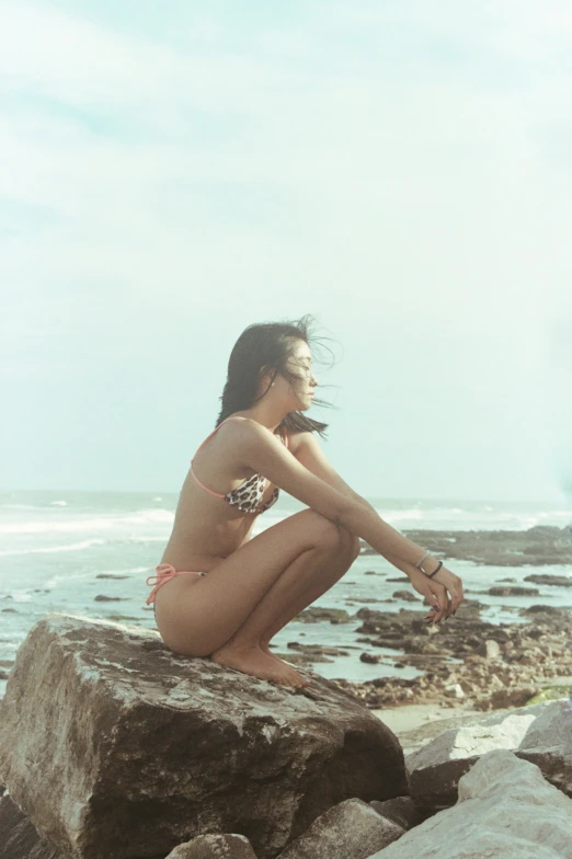 a woman in a bikini sitting on rocks near the ocean