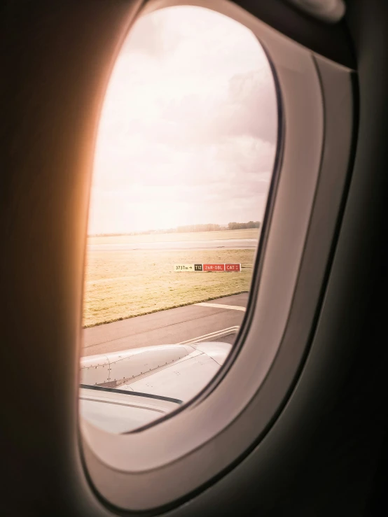 the view out an airplane window shows a dirt runway and field