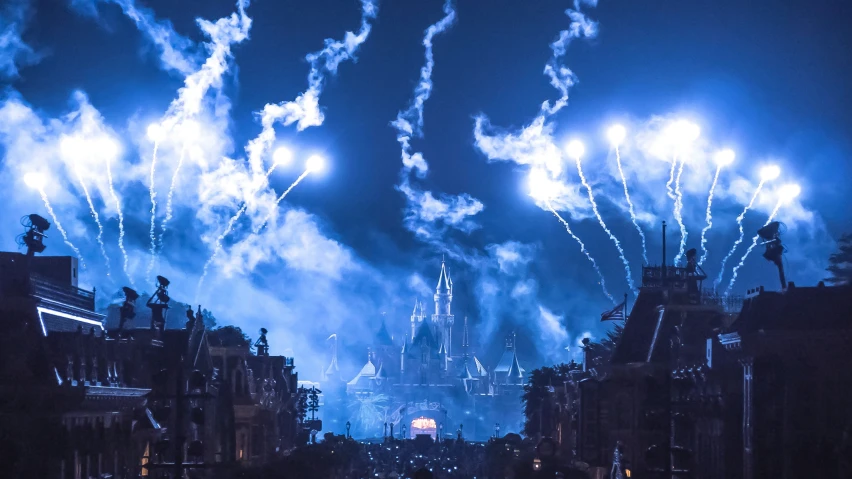 fireworks are set off over the city as a blue castle stands in the distance