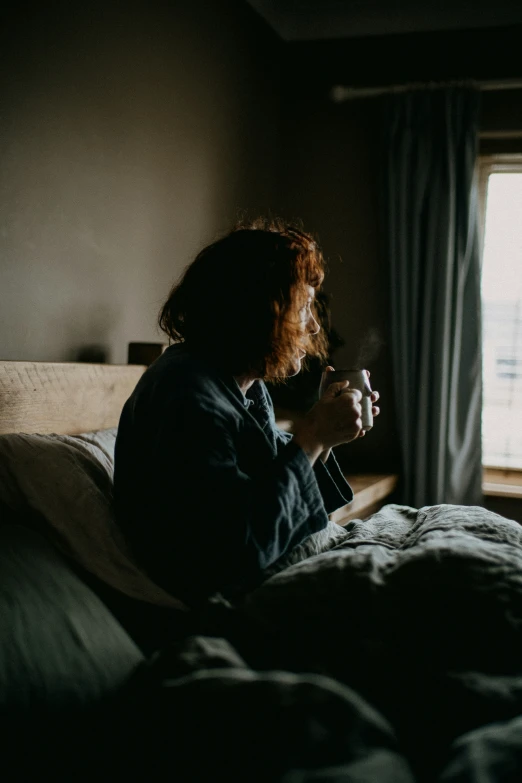 a woman sits on her bed and stares out the window