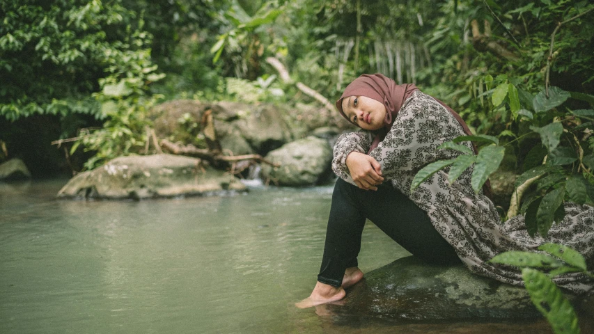 the woman is sitting on rocks by a river