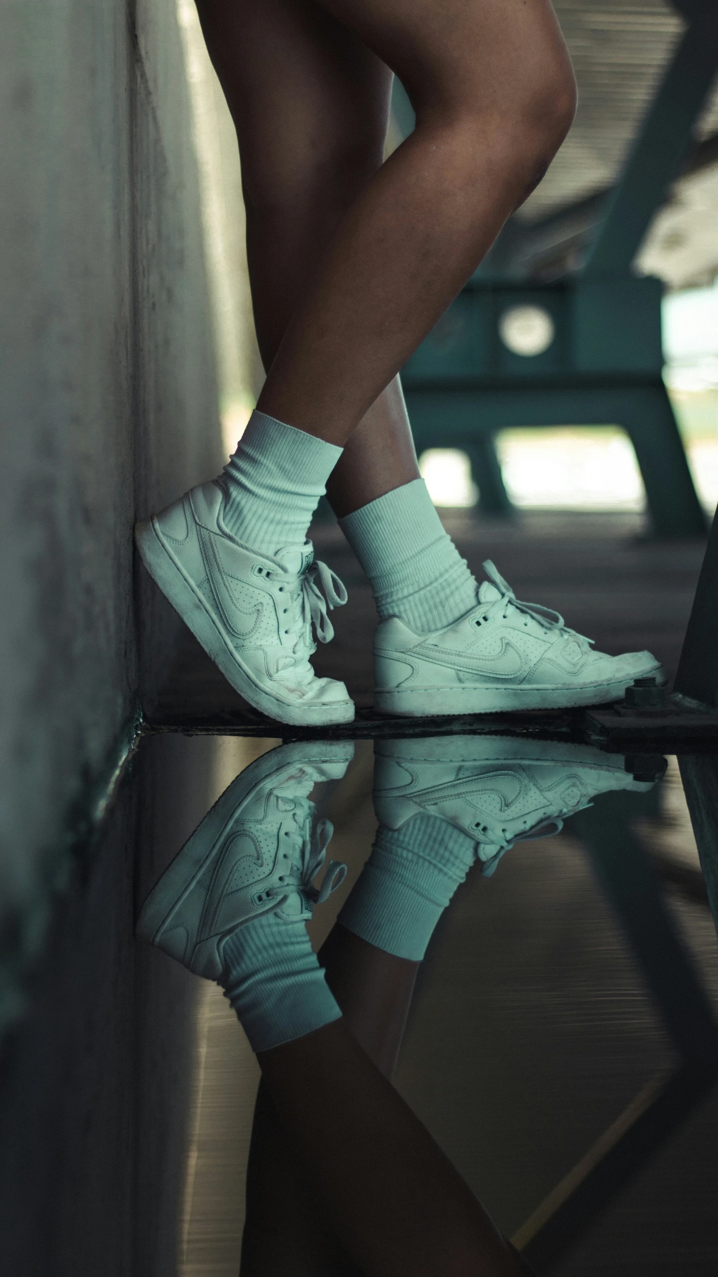 a person's legs in blue sneakers on a reflective surface