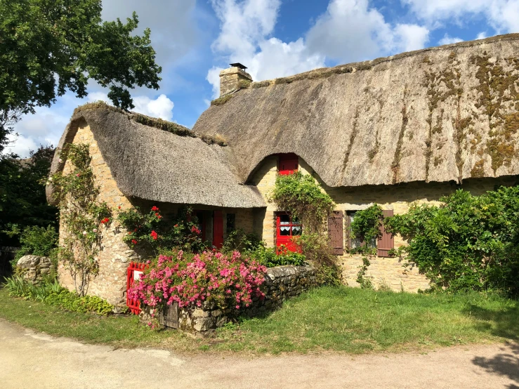 this old thatched cottage has a green roof and flowers in the front yard