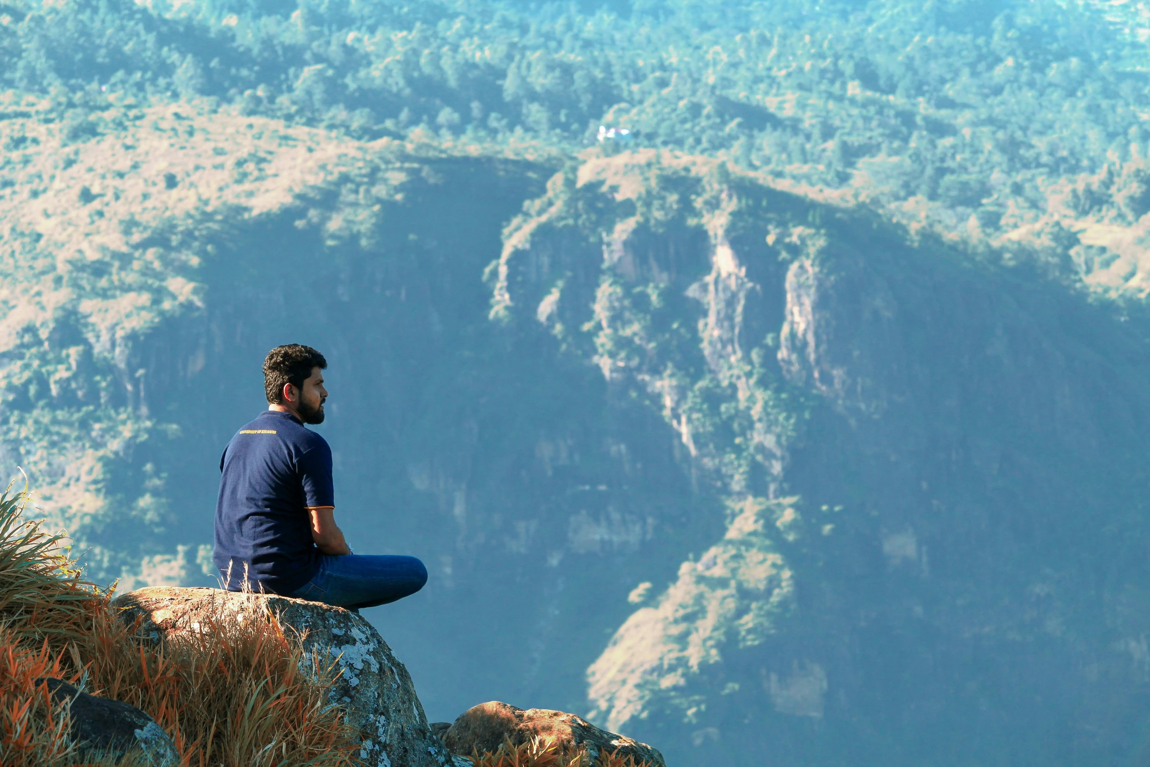 a man sits on a rocky cliff while watching a scenic valley