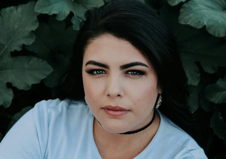 a woman poses for the camera with green foliage behind her